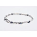 A 9CT WHITE GOLD, SAPPHIRE AND DIAMOND LINE BRACELET, designed with nine oval cut blue sapphires,