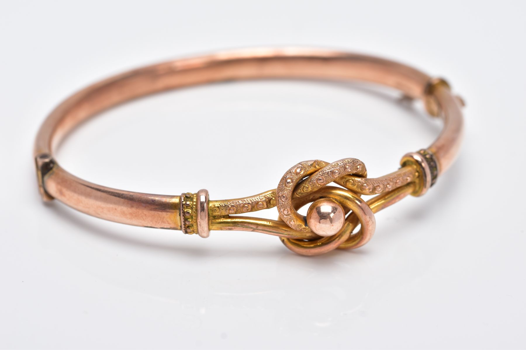 A YELLOW METAL BANGLE, the hinged bangle of a knot and ball openwork design, fitted with a push