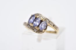 A YELLOW METAL GEM SET RING, of a crossover design, set with three oval cut purple stones assessed