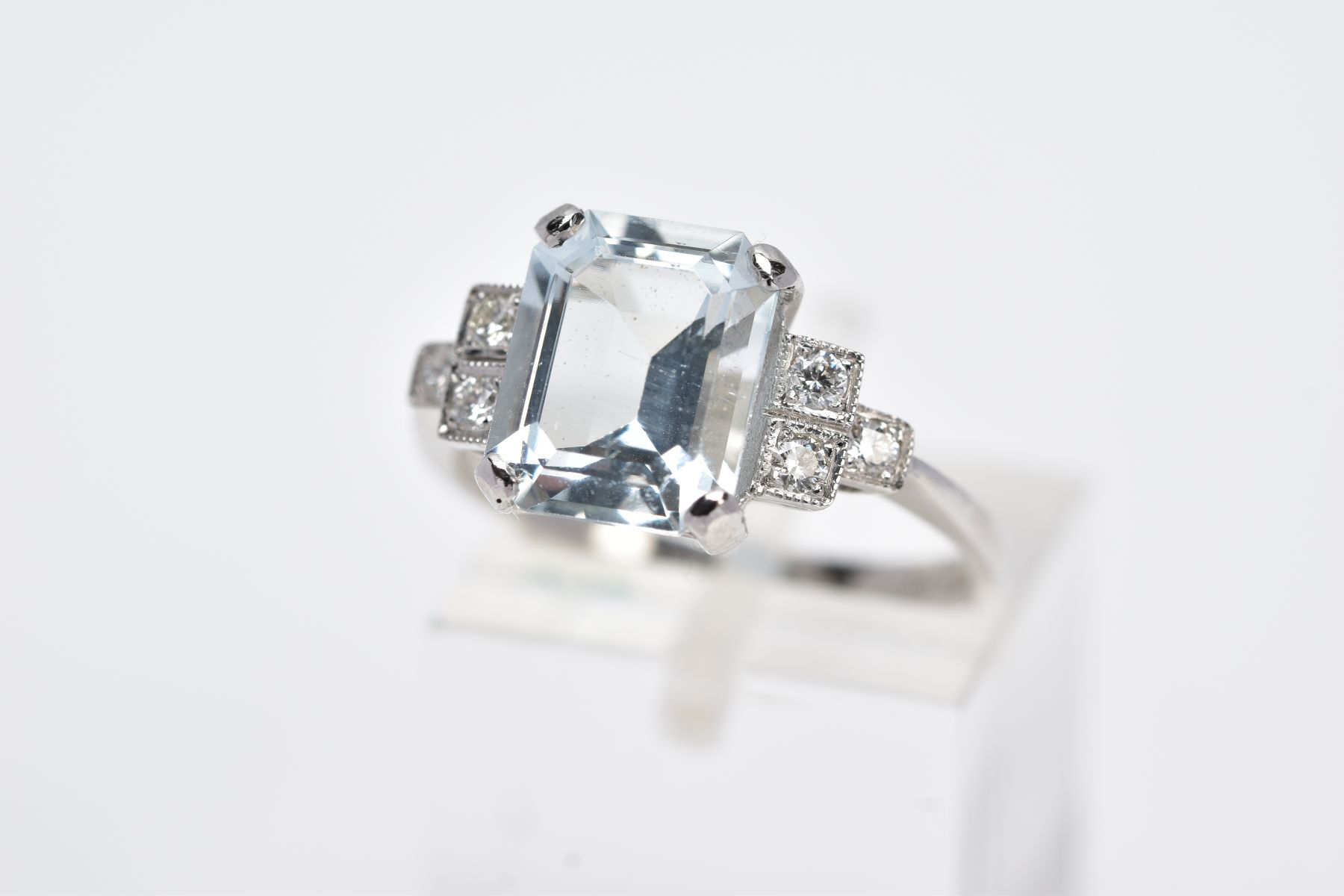 A WHITE METAL AQUAMARINE AND DIAMOND RING, designed with a central claw set, emerald cut aquamarine,