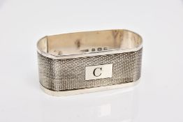 A SHAPED RECTANGULAR SILVER NAPKIN RING, engine turned decoration, initial C engraved to