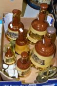A BOX CONTAINING SIX EMPTY BELLS WHISKY DECANTERS, in various sizes, brass ashtrays, brass