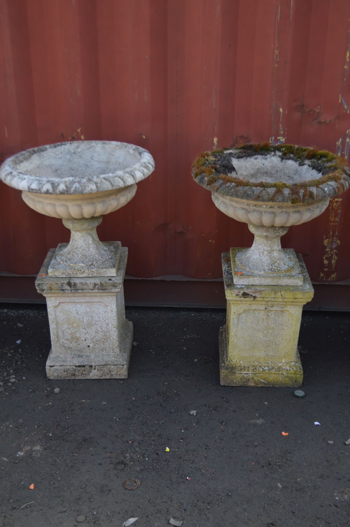 A PAIR OF WEATHERED RECONSTITUTED STONE CAMPANA GARDEN URNS on a separate square plinth base,