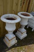 A PAIR OF CAST IRON CAMPANA GARDEN URNS on a separate square plinth, both painted in the colour