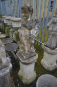 A COMPOSITE GARDEN STATUE OF A SEATED CHERUB/PUTTO, holding a bunch of flowers, on a separate plinth