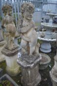 A COMPOSITE GARDEN STATUE OF A SEATED CHERUB/PUTTO, holding a bunch of wheat, on a separate plinth