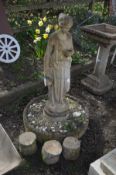 A COMPOSITE WATER FEATURE, of a standing female with flowing robes, on a separate circular stone