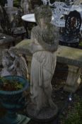 A WEATHERED COMPOSITE GARDEN FIGURE of a semi clad lady with flowing robes, on a circular base,