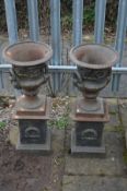 A PAIR OF SMALL CAST IRON CAMPANA URNS, with folate decoration, twin handles on separate plinths,