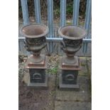 A PAIR OF SMALL CAST IRON CAMPANA URNS, with folate decoration, twin handles on separate plinths,