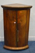 A GEORGIAN STYLE FLAME MAHOGANY BOW FRONT TWO DOOR CORNER CUPBOARD, incorporating older veneers,