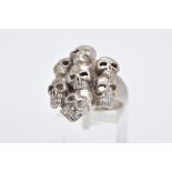 A GENTS WHITE METAL SKULL RING, designed with seven pierced skulls, stamped '925', ring size O,