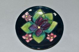 A MOORCROFT POTTERY CIRCULAR PIN DISH DECORATED IN THE VIOLETS PATTERN, on a dark blue ground,