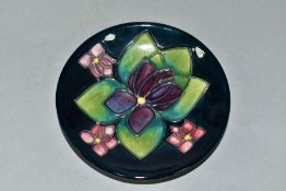 A MOORCROFT POTTERY CIRCULAR PIN DISH DECORATED IN THE VIOLETS PATTERN, on a dark blue ground,