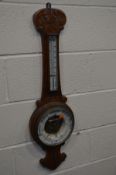 AN EARLY 20TH CENTURY CARVED OAK WHEEL BAROMETER, with a Mercury thermometer and ceramic dial (