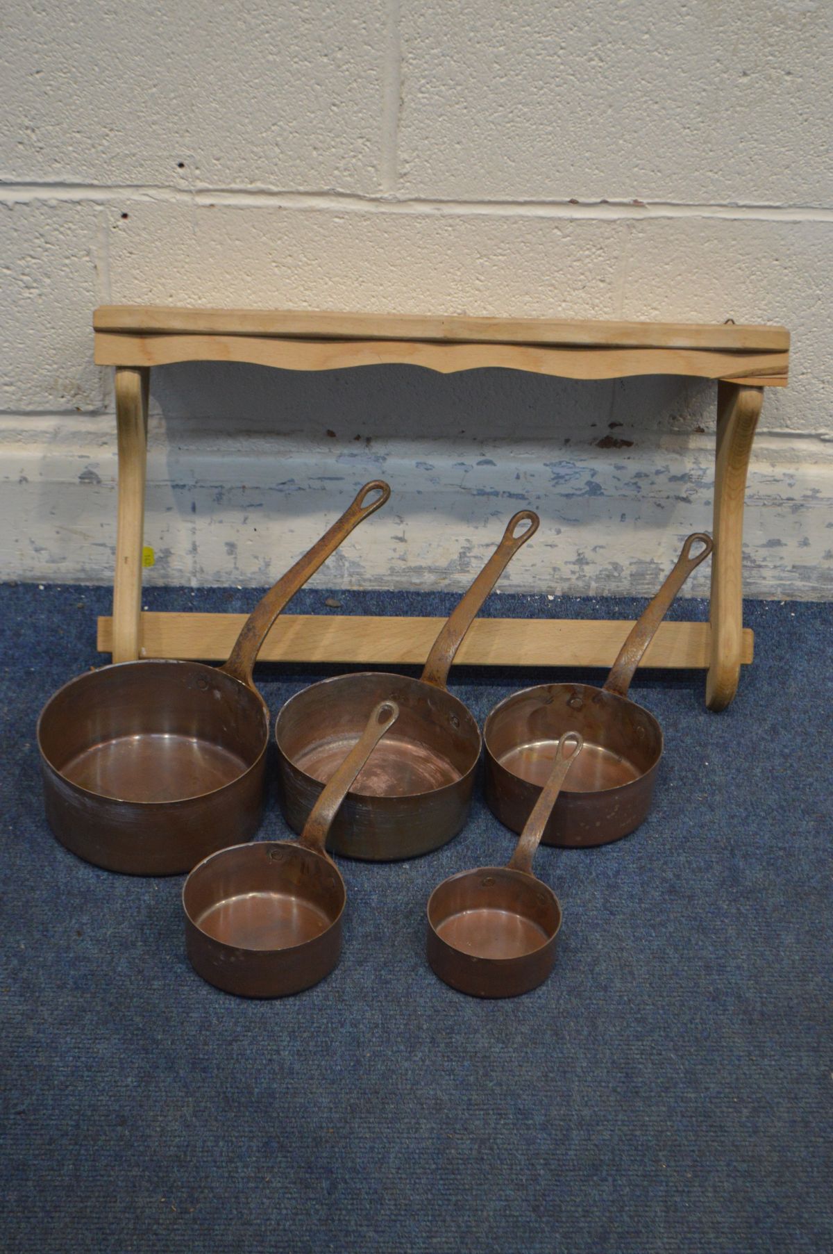 A SET OF FIVE COPPER GRADUATED PANS with hooped iron handles, and a pine hanging wall rack (