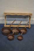A SET OF FIVE COPPER GRADUATED PANS with hooped iron handles, and a pine hanging wall rack (