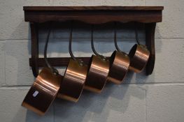 A SET OF FIVE COPPER GRADUATED PANS with hooped iron handles, and a stained pine hanging wall