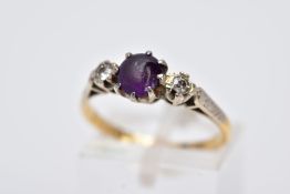 A YELLOW METAL THREE STONE RING, design with a central circular cut purple stone, assessed as paste,