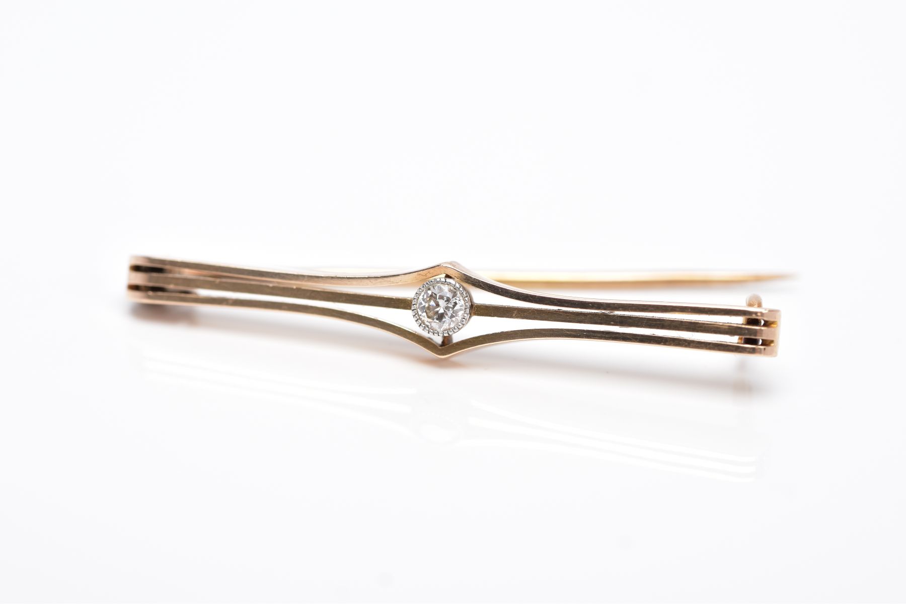 A YELLOW METAL DIAMOND BROOCH, openwork bar brooch set with a round brilliant cut diamond within a