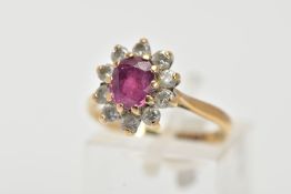 A 9CT GOLD RUBY AND DIAMOND CLUSTER RING, centring on an oval cut ruby, within a claw set, round