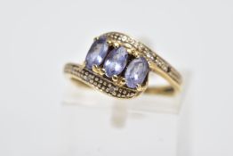 A YELLOW METAL GEM SET RING, of a cross over design, set with three oval cut bluish-purple stones
