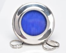 A MINIATURE SILVER PHOTO FRAME AND THREE WHITE METAL RINGS, the frame of a circular form, beaded