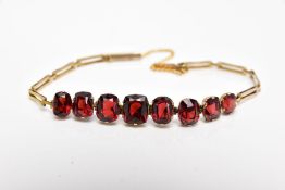 AN EDWARDIAN YELLOW METAL, GARNET SET BRACELET, designed with a row of graduated cushion and oval