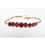 AN EDWARDIAN YELLOW METAL, GARNET SET BRACELET, designed with a row of graduated cushion and oval