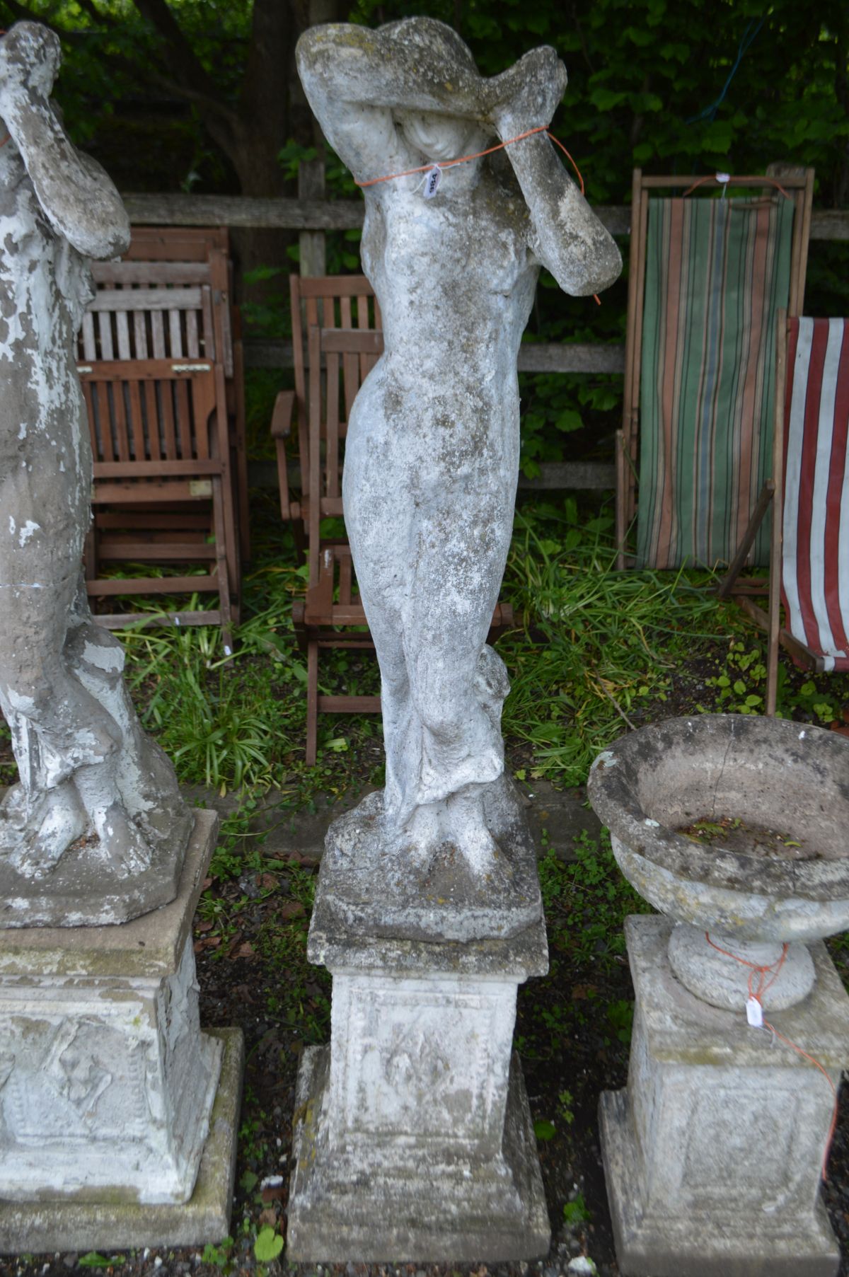 A WEATHERED COMPOSITE GARDEN STATUE of a lady in flowing robes, on a separate matched plinth,