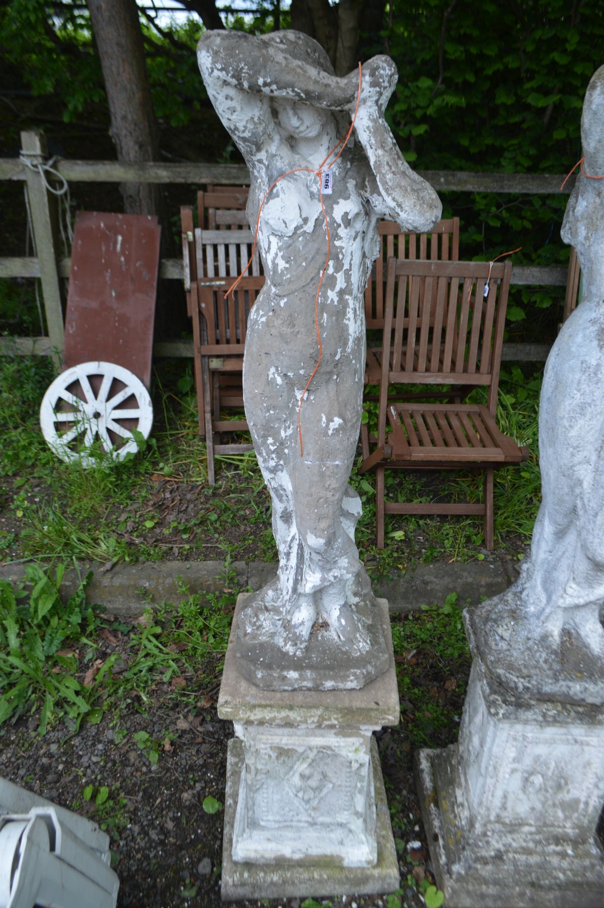 A WEATHERED COMPOSITE GARDEN STATUE of a lady in flowing robes, on a separate matched plinth,