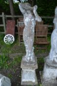 A WEATHERED COMPOSITE GARDEN STATUE of a lady in flowing robes, on a separate matched plinth,