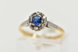 A YELLOW METAL CLUSTER RING, designed with a central, circular cut blue sapphire within a surround