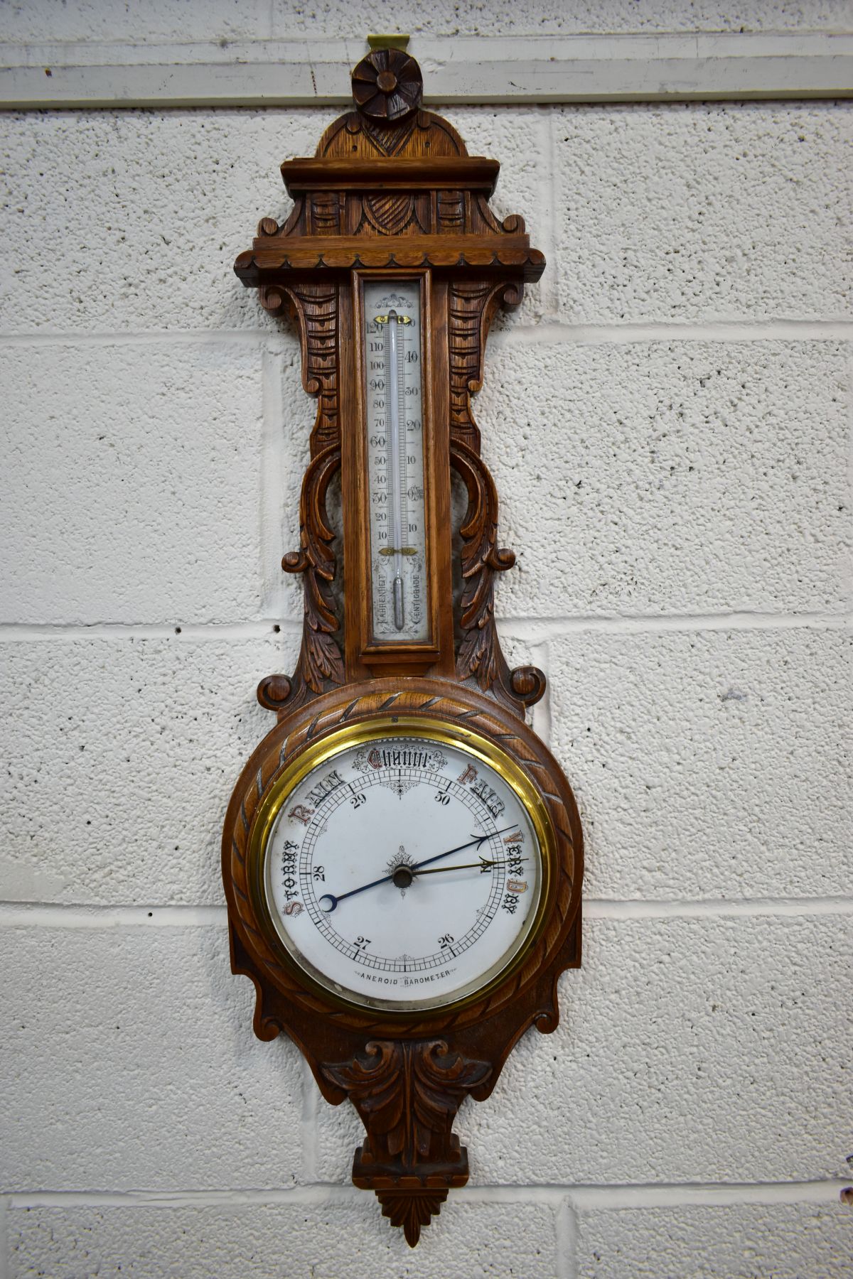 A LATE VICTORIAN CARVED OAK ANEROID BAROMETER, with mercury thermometer and working blued indicator,