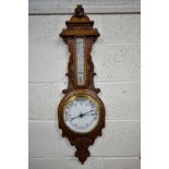 A LATE VICTORIAN CARVED OAK ANEROID BAROMETER, with mercury thermometer and working blued indicator,