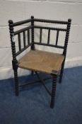 AN EARLY 20TH CENTURY EBONISED ARTS AND CRAFTS BOBBIN TURNED CORNER CHAIR with a rush seat