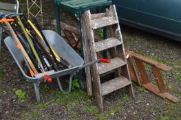 A GALVANISED WHEELBARROW, containing a collection of garden hand tools, two wooden step ladders