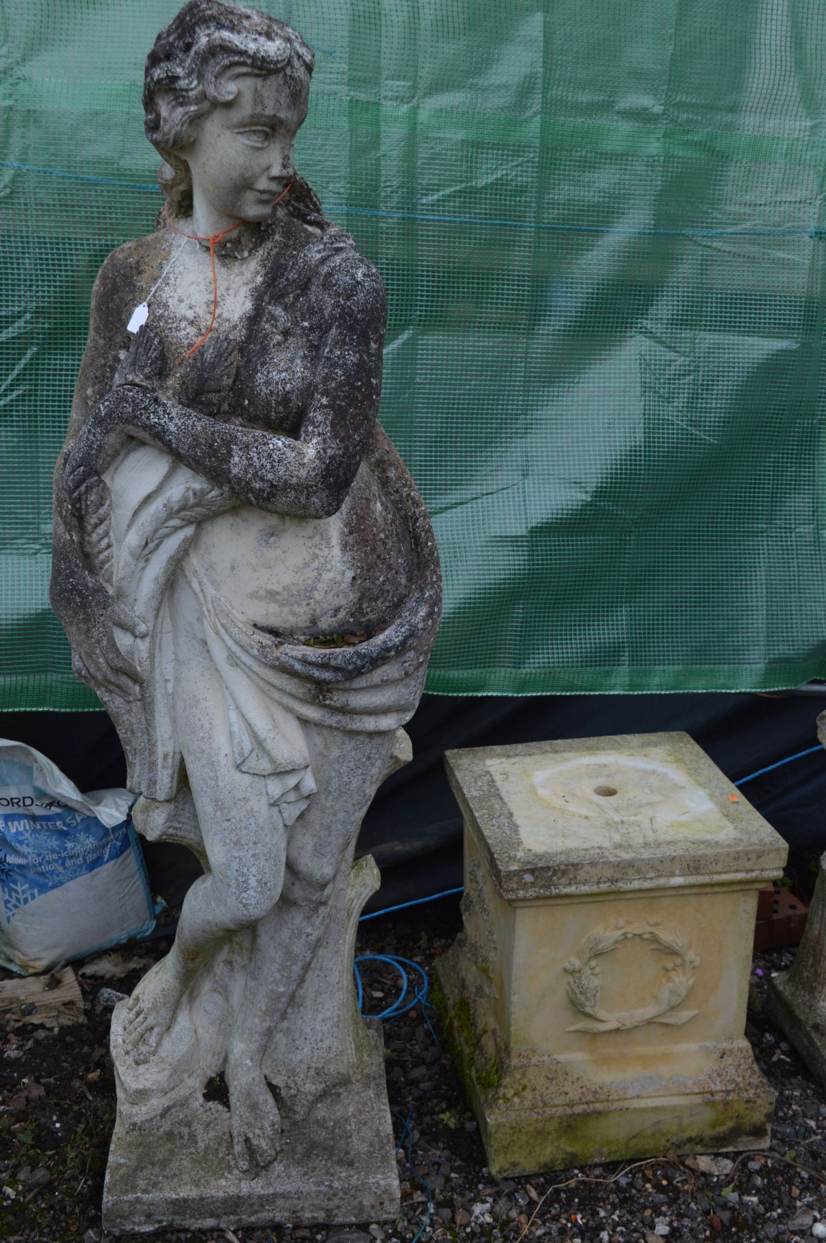 A LARGE WEATHERED COMPOSITE GARDEN STATUE of a semi clad lady in flowing robes, collecting the