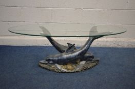 AN OVAL GLASS TOP COFFEE TABLE SUPPORTED ON TWO RESIN DOLPHINS lying on a sea bed, width 120cm x