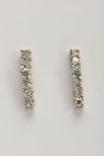 A PAIR OF WHITE METAL DIAMOND DROP EARRINGS, each designed as a wavy line drop set with seven claw