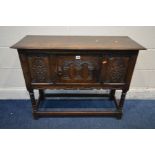 A REPRODUCTION OAK CREDENCE CABINET with a single carved panel cupboard door flanked by carved