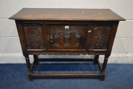 A REPRODUCTION OAK CREDENCE CABINET with a single carved panel cupboard door flanked by carved