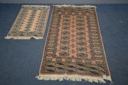 A WOOLEN PINK GROUND TEKKE RUG, 153cm x 93cm and a matching smaller rug (2)