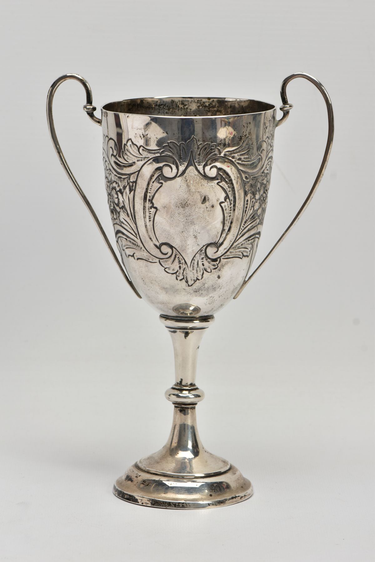 A SILVER TROPHY CUP, double scroll handles, embossed floral and foliate design, with a vacant