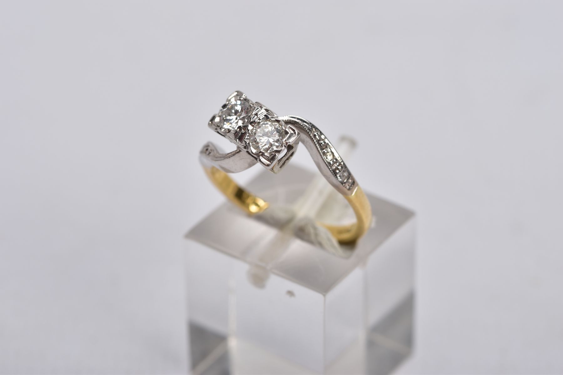 AN 18CT GOLD DIAMOND CROSS OVER RING, designed with two asymmetrical set round brilliant cut