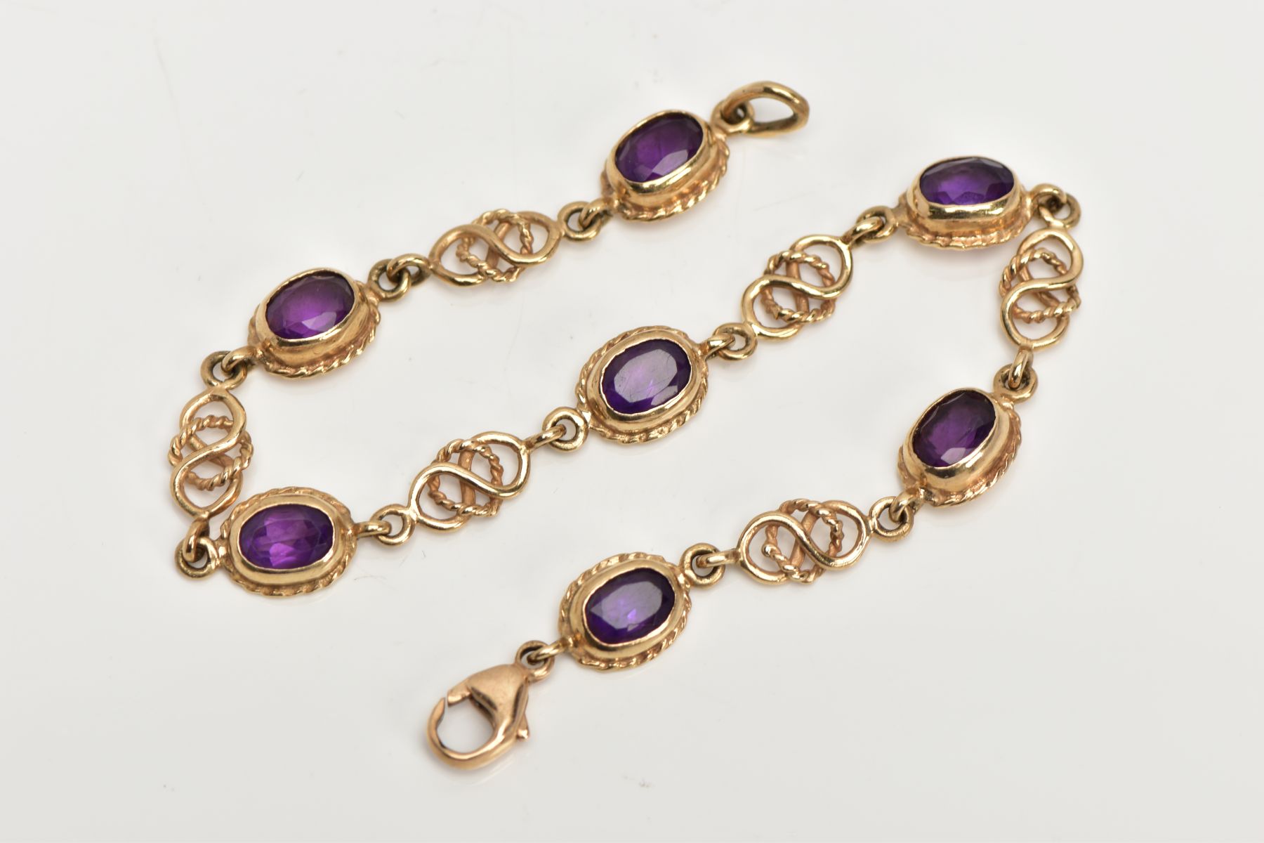 A 9CT GOLD AMETHYST LINE BRACELET, designed with seven oval cut amethysts, each with a collet