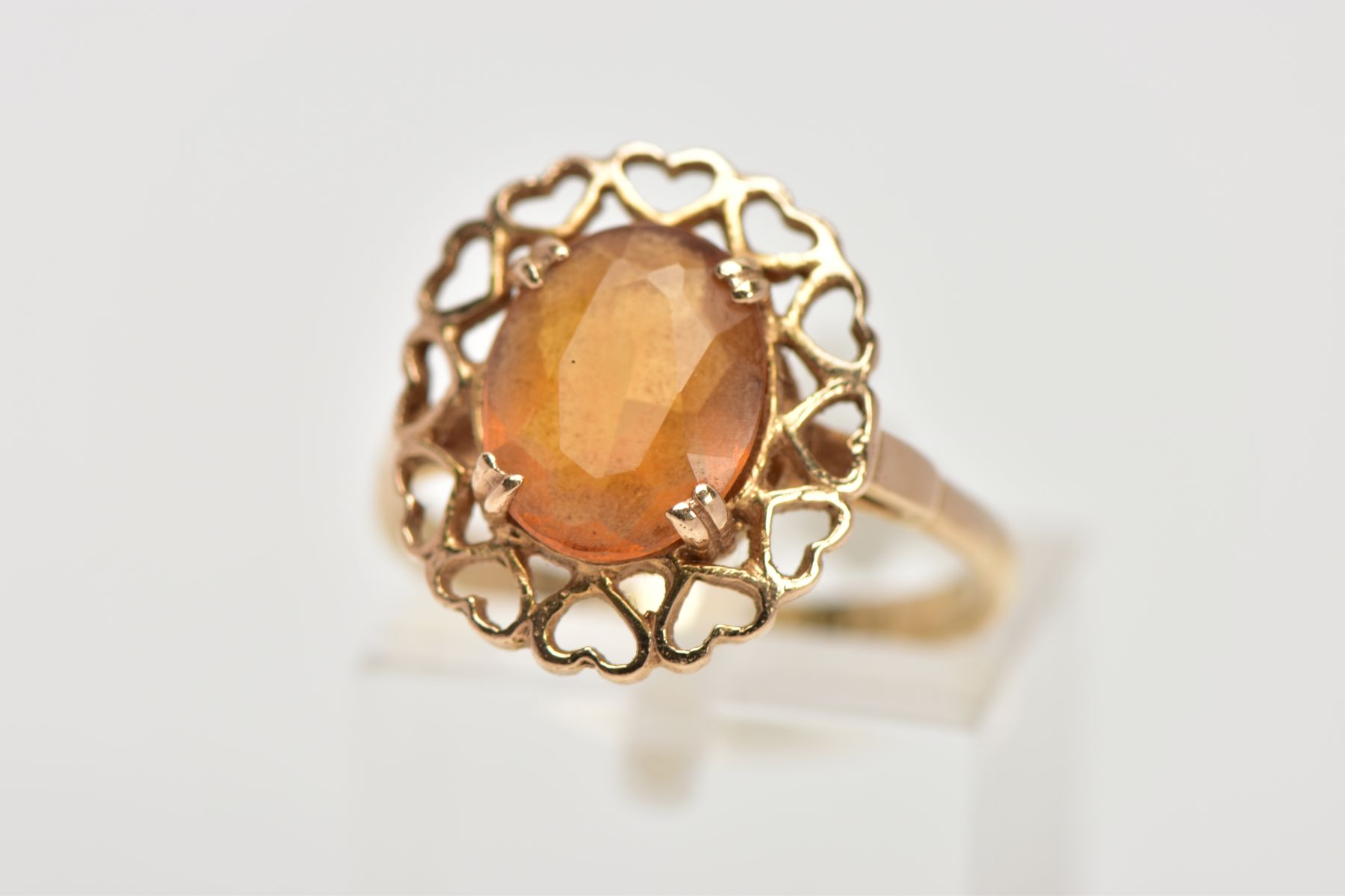 A YELLOW METAL CITRINE RING, designed with a claw set oval cut citrine, within an openwork heart