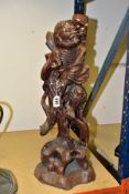 A 20TH CENTURY CHINESE CARVED HARDWOOD FIGURE OF A JOVIAL MAN, holding a staff in both hands, a