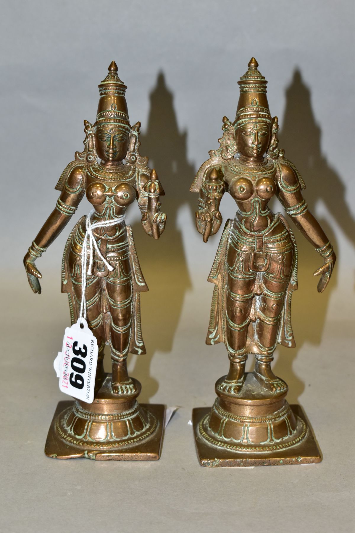 A NEAR PAIR OF BRONZE FIGURES OF PARVATI HOLDING A LOTUS FLOWER, cast on a circular plinth with
