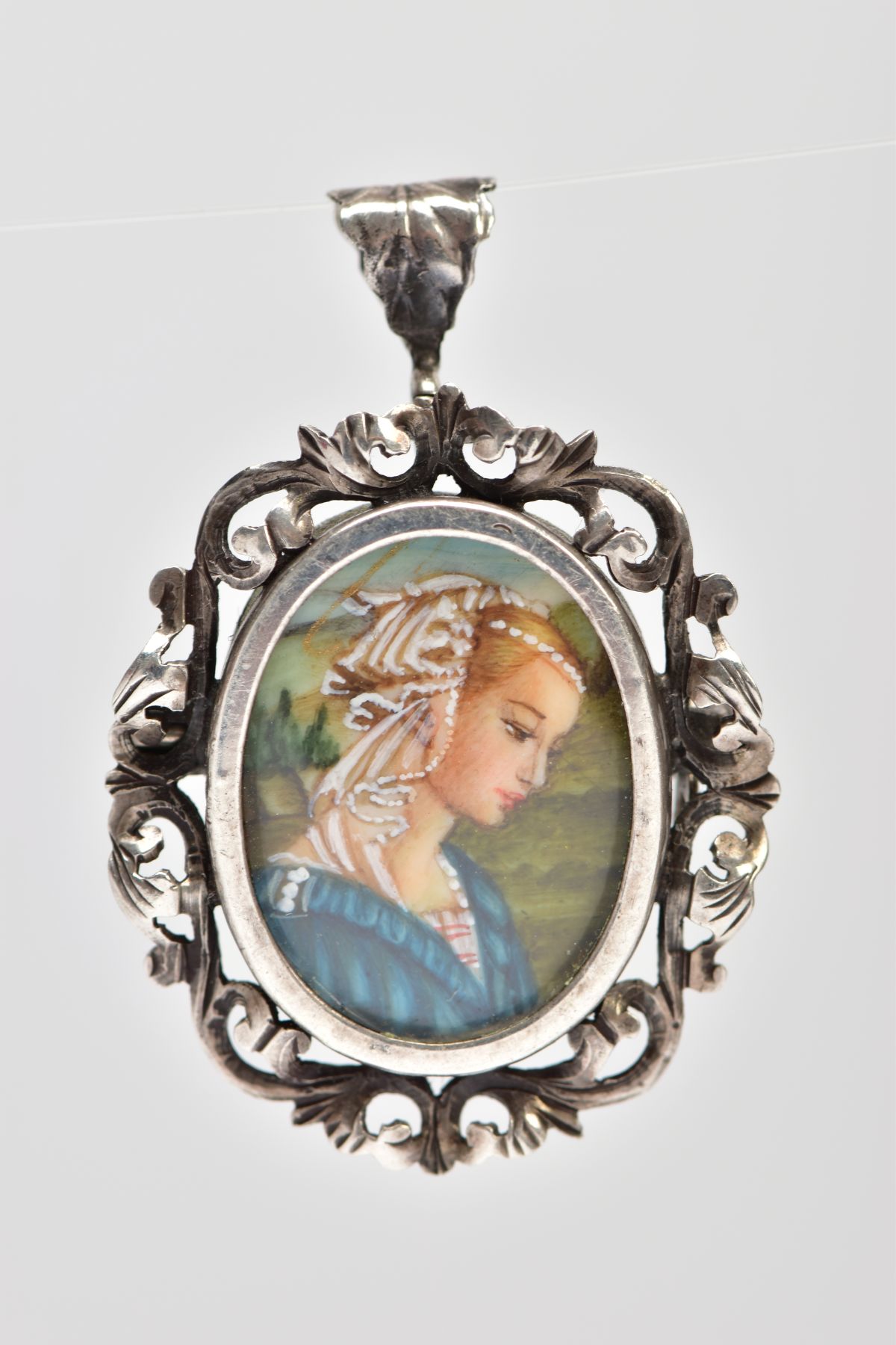 A PENDANT/BROOCH, of oval outline with central hand painted portrait of a lady within a scrolling
